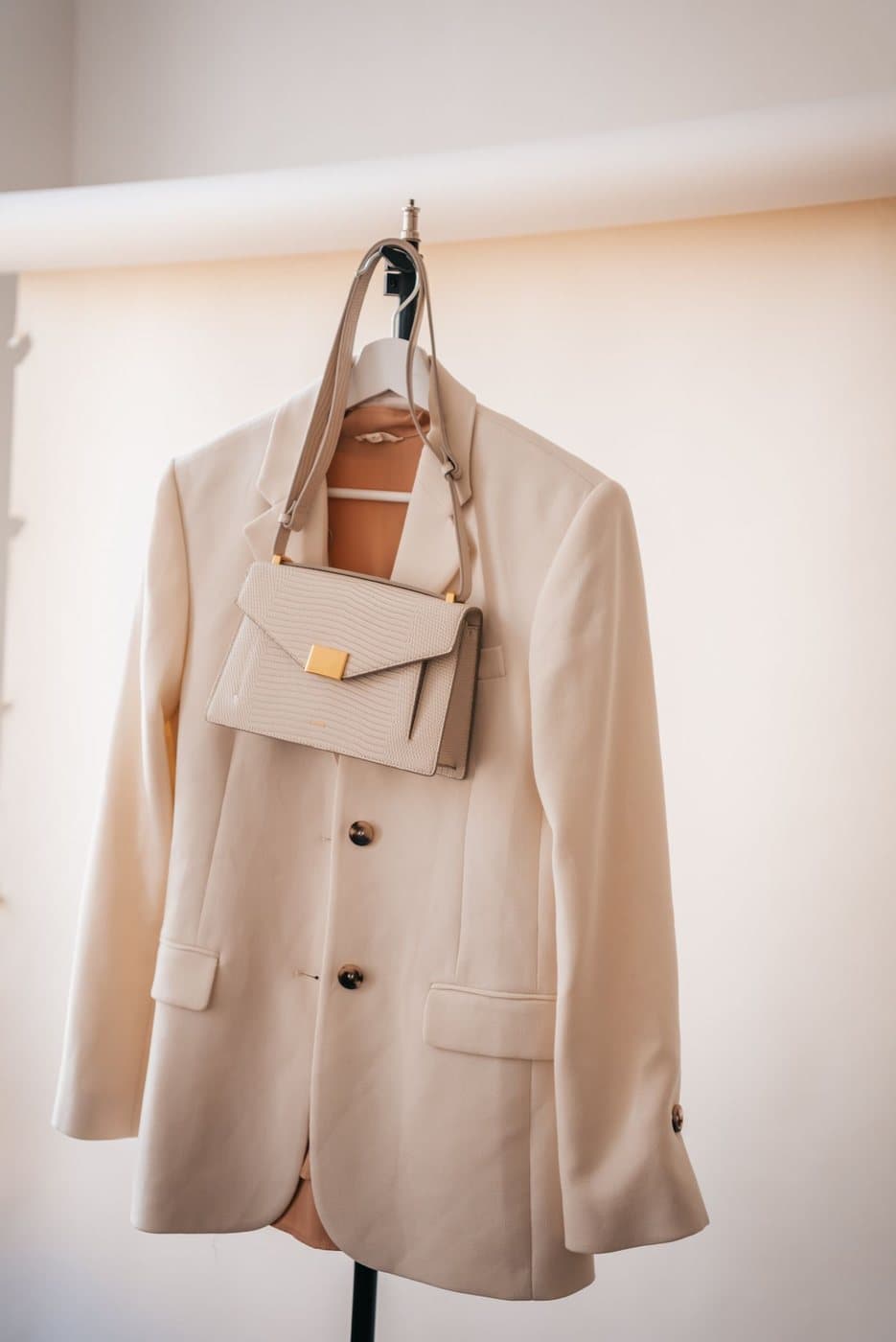 A beige blazer and a handbag hanging on a wall
